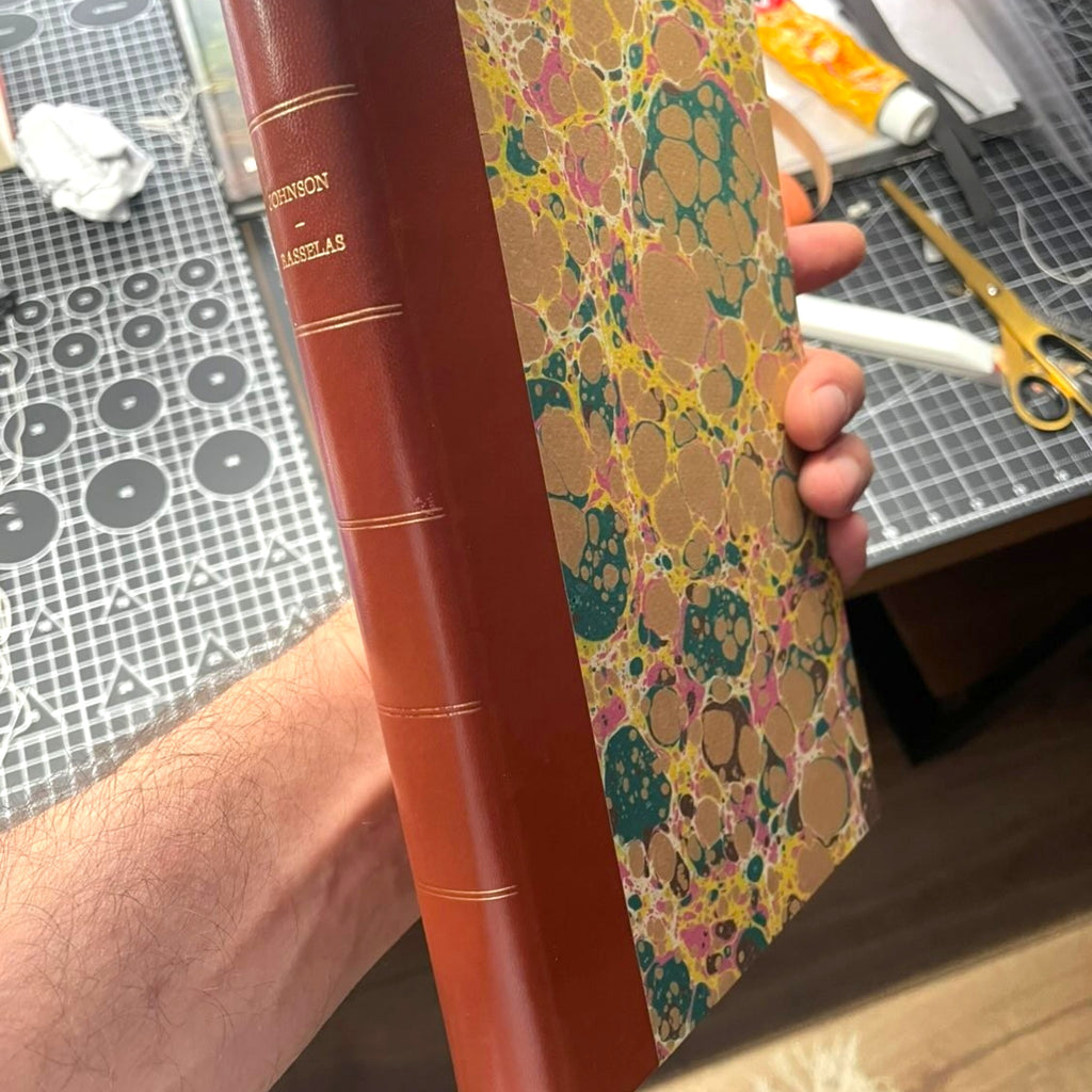Samuel Johnson Rasselas fine press edition, handcrafted half-leather binding with marbled paper boards, traditional bookbinding workshop and artisan craftsmanship by Woodbank Press.
