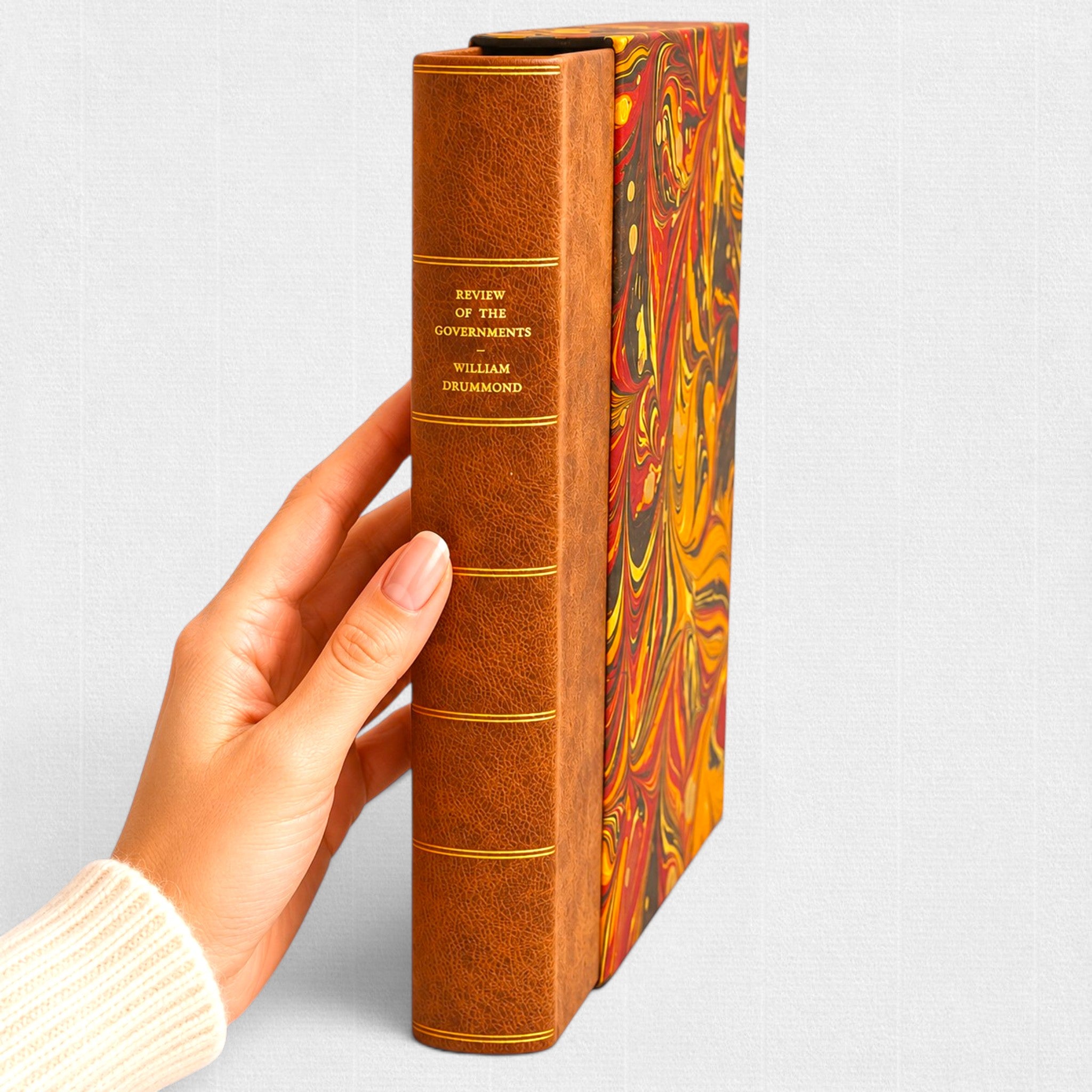 Hand holding A Review of the Governments of Sparta and Athens by Sir William Drummond, showcasing the full leather binding and marbled slipcase of this limited fine press edition by Woodbank Press.