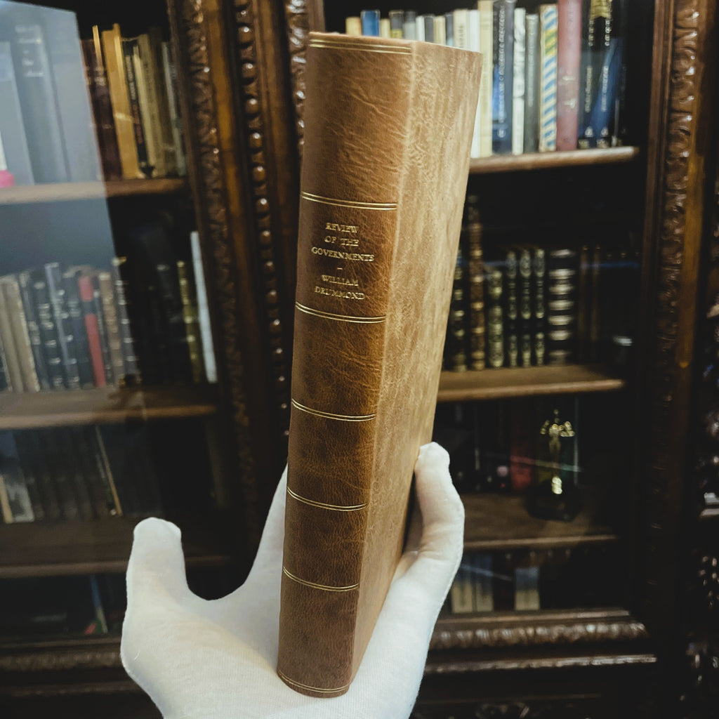 Hand holding A Review of the Governments of Sparta and Athens by Sir William Drummond, limited hand-bound fine press edition by Woodbank Press, displayed before a private library.